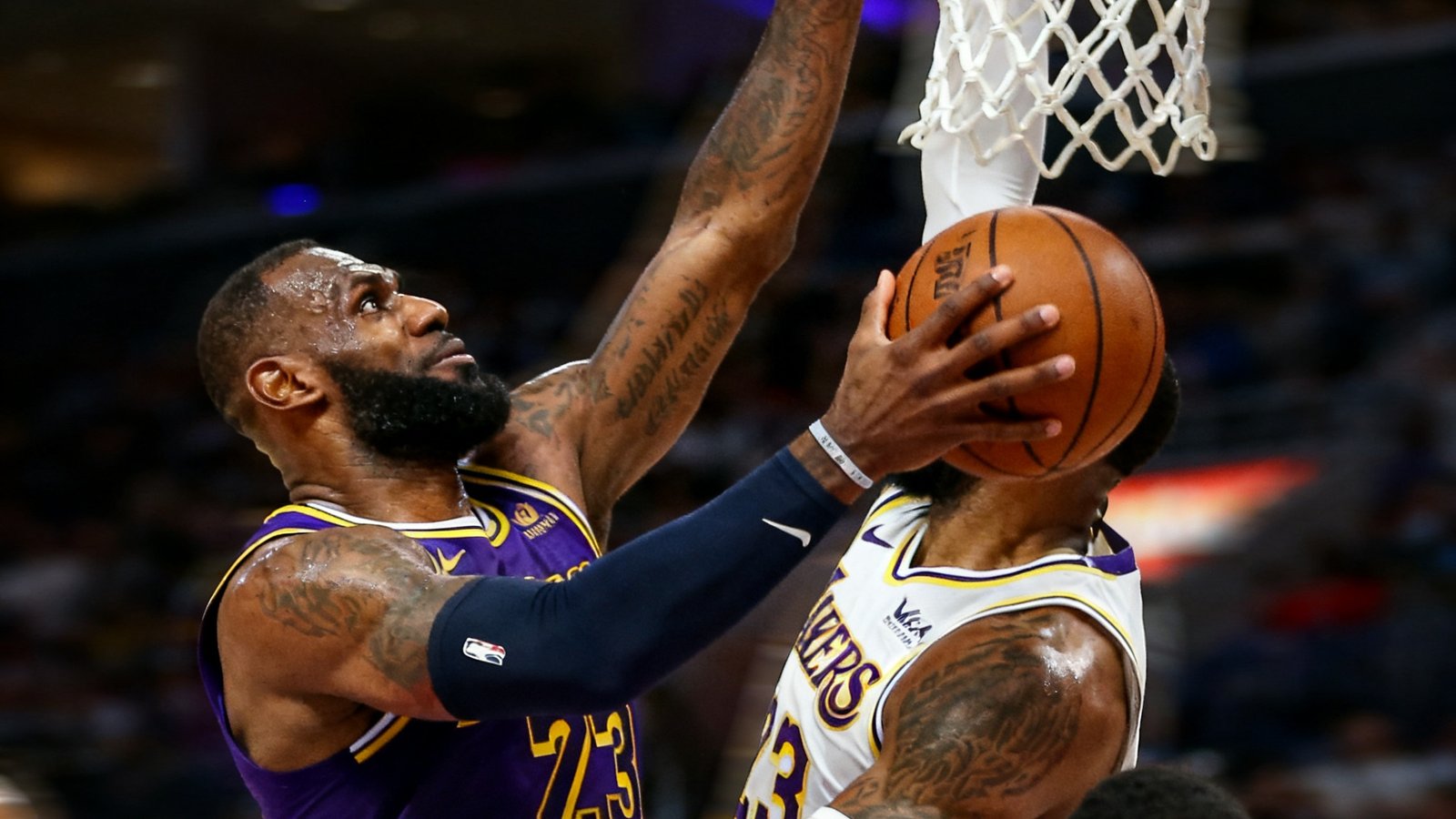 NBA赛场勒布朗詹姆斯突破上篮的精彩特写，防守球员奋力跳起试图封盖，篮筐近在咫尺